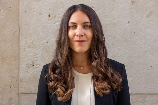 Person mit einem Blazer steht vor grauer Wand.