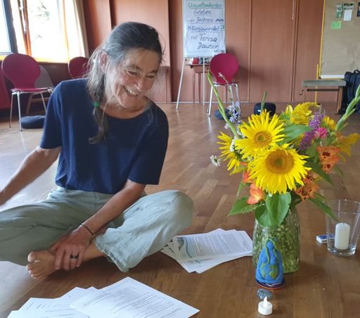 Lachende Frau sitzt auf Holzboden.
