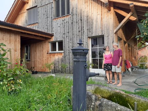 Mann und Frau stehen in kurzen Hosen vor Holzhaus.